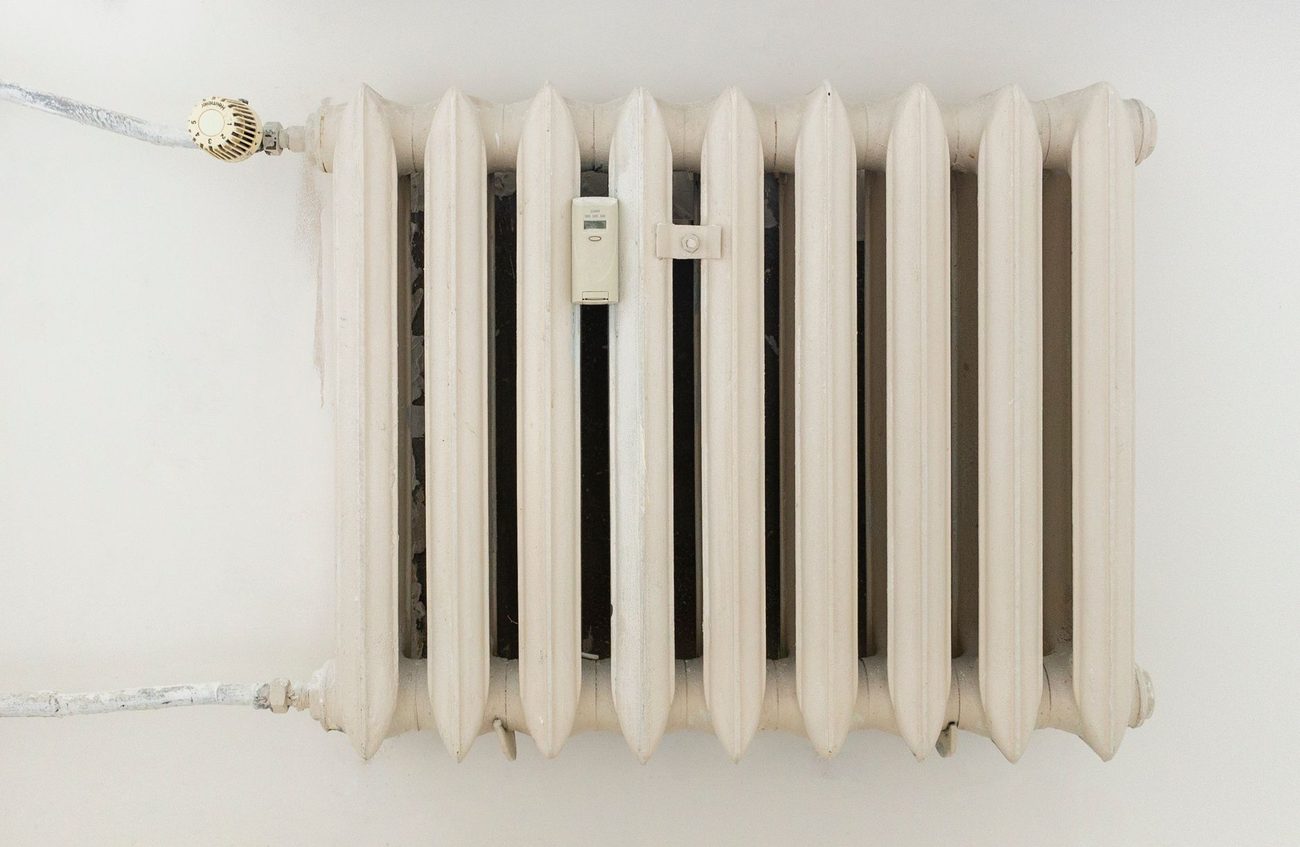 Oude witte radiator met thermostaatknop in een woonkamer